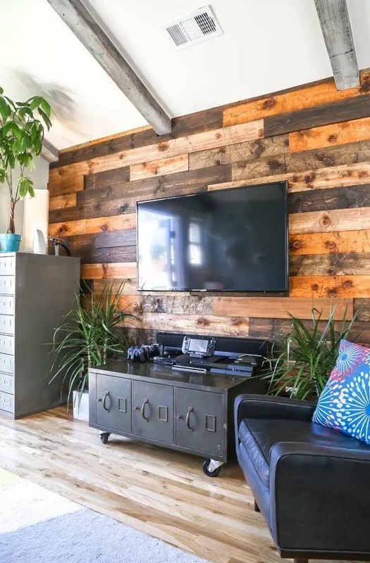 A weathered and stained wood accent wall softens the industrial inspired living room with vintage touches