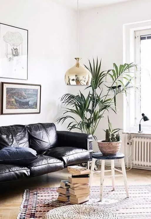 a gorgeous contemporary living room with a black leather sofa, stacks of books, potted plants and a chic gallery wall