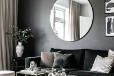 70 a chic and dramatic living room with a black accent wall, a black velvet sofa, chic glass coffee tables, pendant bulbs and a round mirror