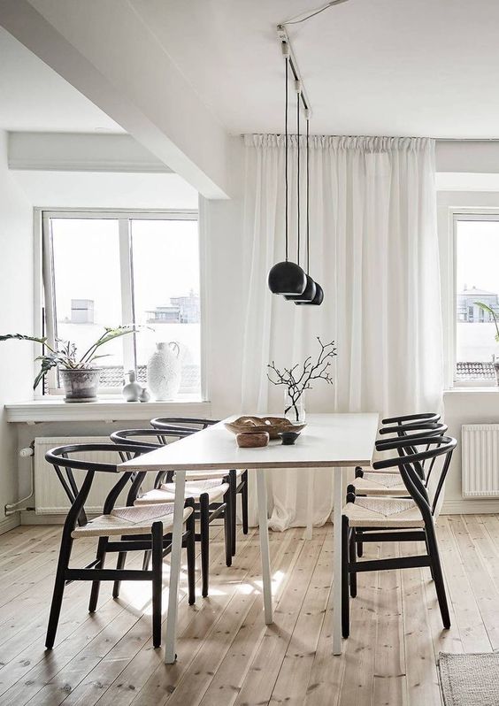 A Nordic dining space with a light stained table, black wishbone chairs and a row of black pendant lamps is cool