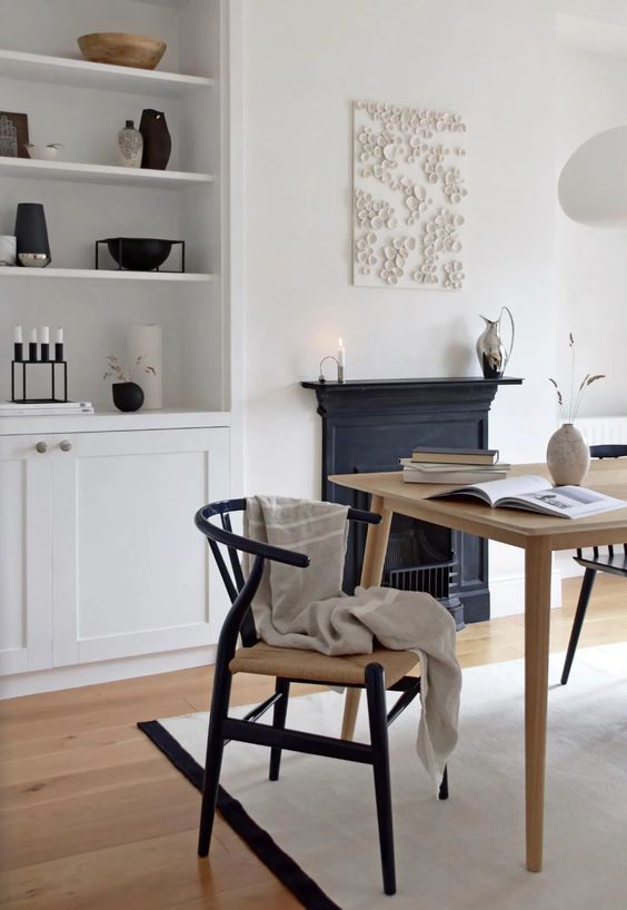 a Nordic dining space with built-in storage units, a vintage non-working fireplace, a stained table and black wishbone chairs