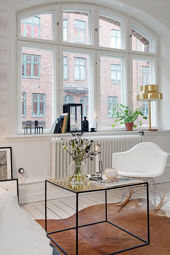 a Nordic space with a white sofa, a chic coffee table, a white Eames rocker, some books and lamps on the windowsill