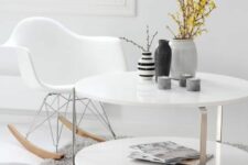 a Nordic space with a white tiered coffee table, a white Eames rocker, a grey rug and a grey pillow