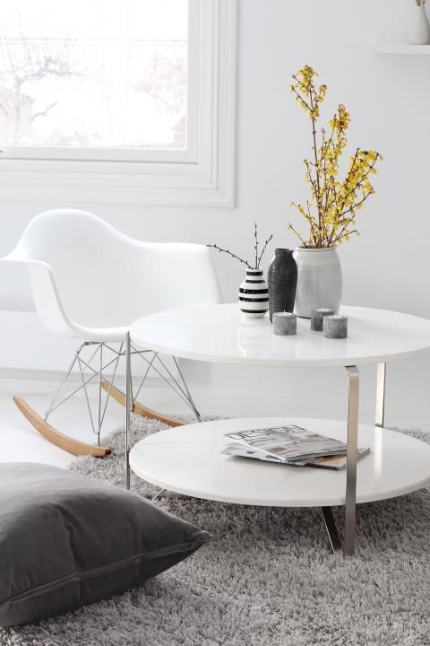 a Nordic space with a white tiered coffee table, a white Eames rocker, a grey rug and a grey pillow