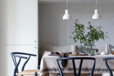 a Scandi dining space with a storage unit and a built-in seat, a dining table and navy wishbone chairs, white pendant lamps