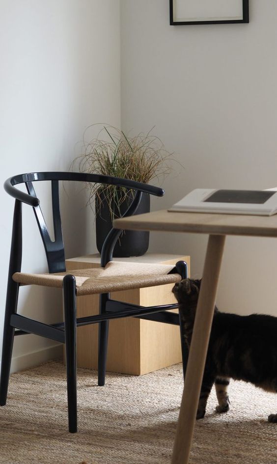 A Scandinavian dining and working space with a light stained table, a black wishbone chair, a stand with a black plantern and a rug