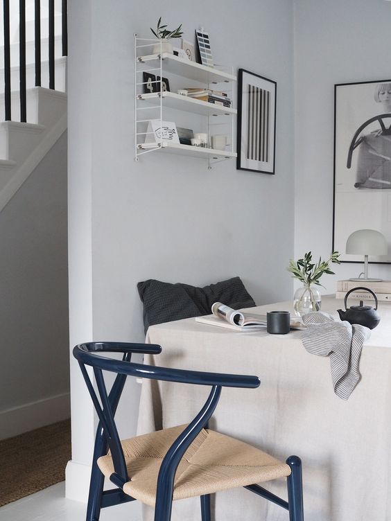 a Scandinavian dining room with a table, a navy wishbone chair, a small white storage unit and some art