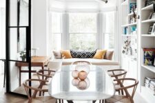 a Scandinavian dining room with a windowsill seat, large bookcases, an oval table and stained wishbone chairs