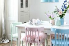 a Scandinavian dining space with a white buffet, a white dining table and pastel chairs, a blue pendant lamp and floral porcelain