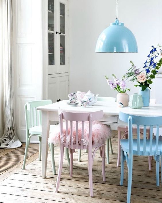 a Scandinavian dining space with a white buffet, a white dining table and pastel chairs, a blue pendant lamp and floral porcelain
