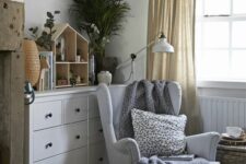a Scandinavian kids’ room with a white IKEA Strandmon chair styled with a pillow and a blanket and a woven chest as a side table