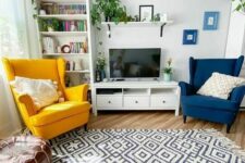 a Scandinavian living room with a bookcase, a TV unit, a navy and yellow Strandmon chair, a printed rug and a leather pouf plus potted greenery