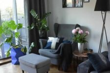 a Scandinavian living room with a grey Strandmon chair and an ottoman, a black sofa, potted plants, a black floor lamp and a gallery wall