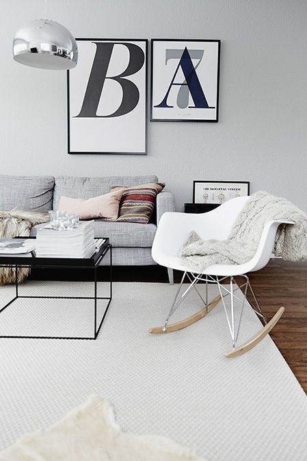 a Scandinavian living room with a grey sofa, a black coffee table, a white Eames rocking chair, black and white artwork