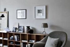 a Scandinavian living room with stained bookshelves, a grey Wumb chair and ottoman, some artwork and lamps