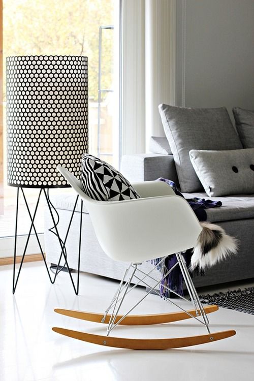 a Scandinavian space with a grey sofa and pillows, a white Eames rocker, a large printed floor lamp and a rug