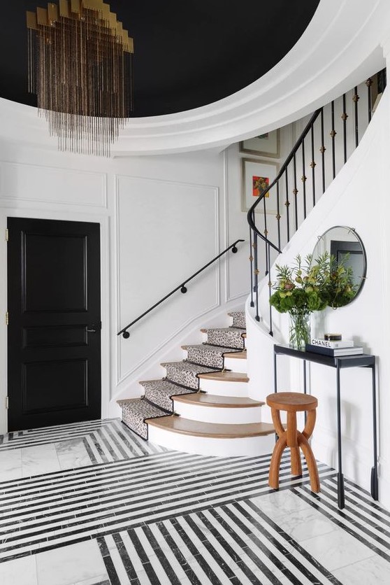 a beautiful black and white entryway with black doors and a ceiling, a black and white marble floor, a black console table and a gorgeous chandelier