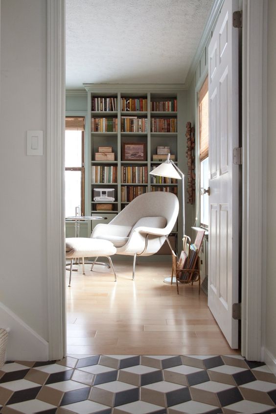 a beautiful home library with light green bookcases and shelves, a creamy Wumb chair and ottoman, a magazine stand