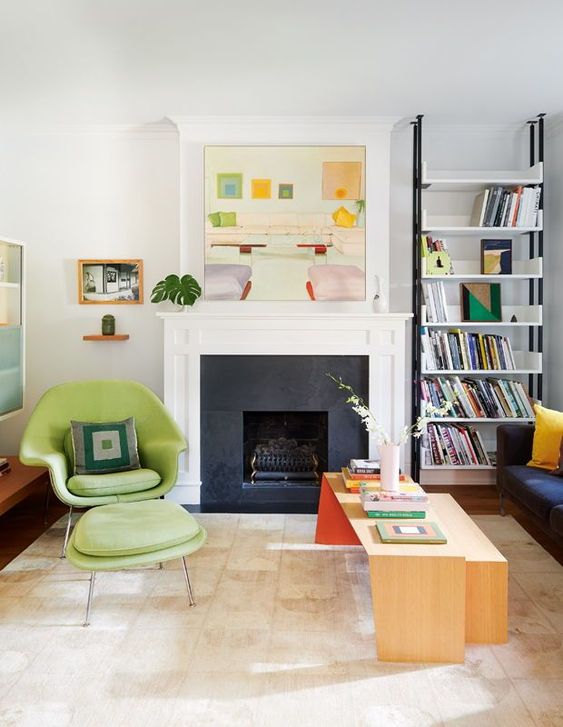 A beautiful mid century modern living room with a fireplace, bookshelves, a green Wumb chair with an ottoman, a duo of coffee tables