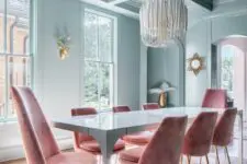 a beautiful pastel blue dining room with a coffeered ceiling, large windows, a corner niche, a blue table and pink chairs
