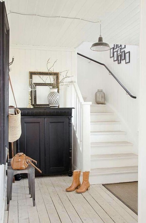 A black and white entryway with a black built in cabinet, artworks, metal stools, empty frames and a pendant lamp