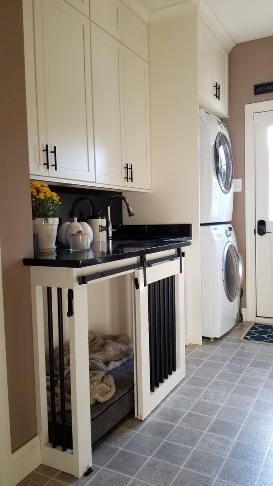A black and white farmhouse laundry with cabinets and a built in dog crate plus stacked appliances