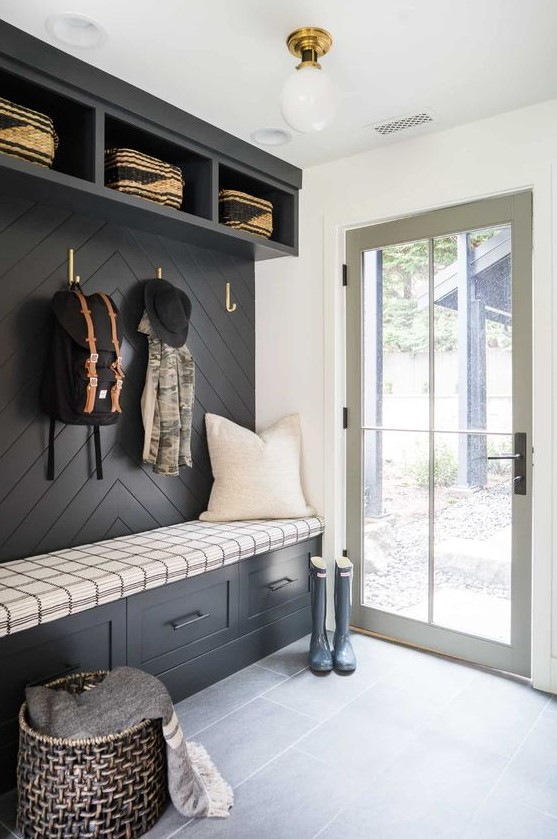 a black and white farmhouse mudroom with a black accent wall and built-in storage units, a basket for storage and a glass door