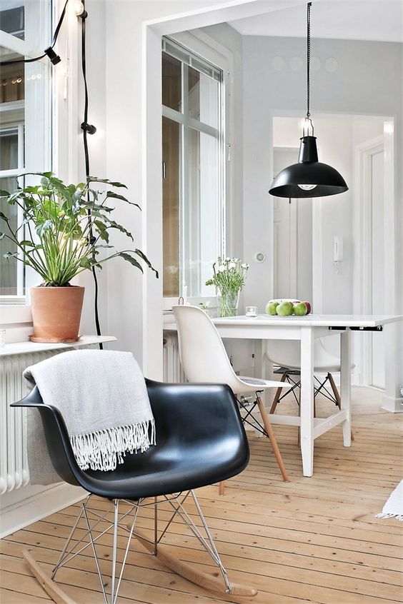 a black and white space with a white table and two Eames chairs plus a black Eames chair and a black pendant lamp
