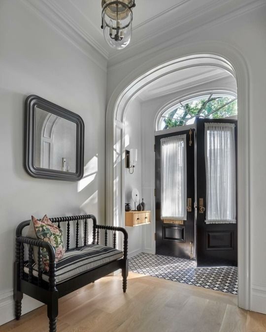 a black and white vintage entryway with black doors, a black and white tile floor, a floating console, a black bench with a cushion
