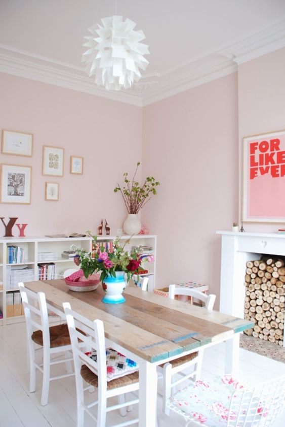 a blush dining room with a non-working fireplace, a reclaimed wood table, rustic chairs, a large bookshelf and a gallery wall