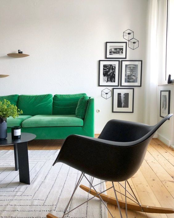 a bold Scandinavian living room with a green sofa, a black Eames rocking chair, a black coffee table and black and white gallery wall