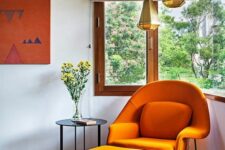 a bold corner window nook with an orange Wumb chair and ottoman, a side table, faceted pendant lamps and woven shades