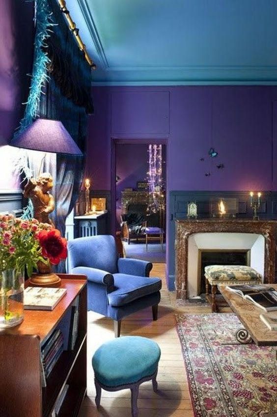 a bold living room with a blue ceiling, purple walls, a fireplace with a stone surround, a navy chair and a green stool, some lamps