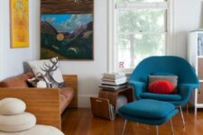 a bold mid-century modern living room with rust-colored loveseat, a blue Wumb chair with an ottoman, a curved shelf and pillows