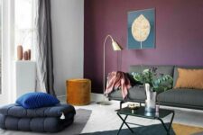 a bright living room with a purple accent wall, a grey sofa, black poufs, a coffee table, a floor lamp and a pouf