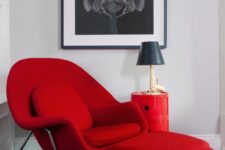 a bright nook with a black and white artwork, a hot red Wumb chair and ottoman, a side table and a blue rug