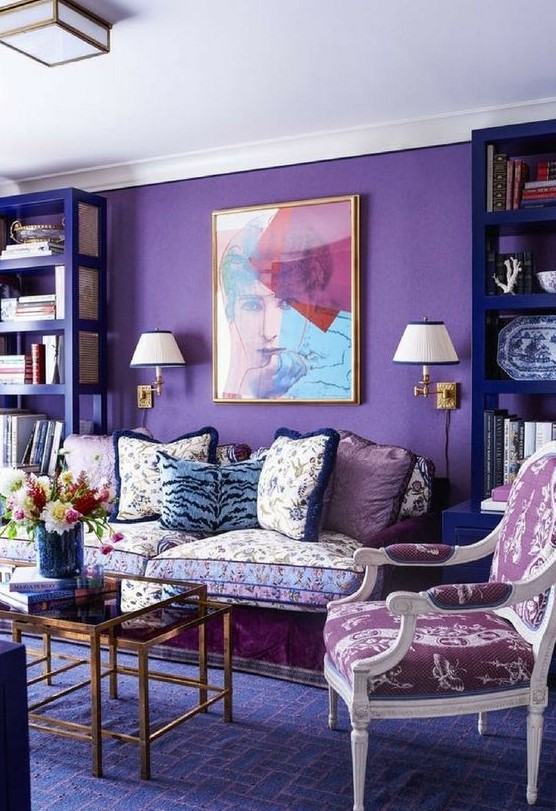 a bright whimsical interior with a purple accent wall, violet bookcases, floral print seating furniture and glass coffee tables