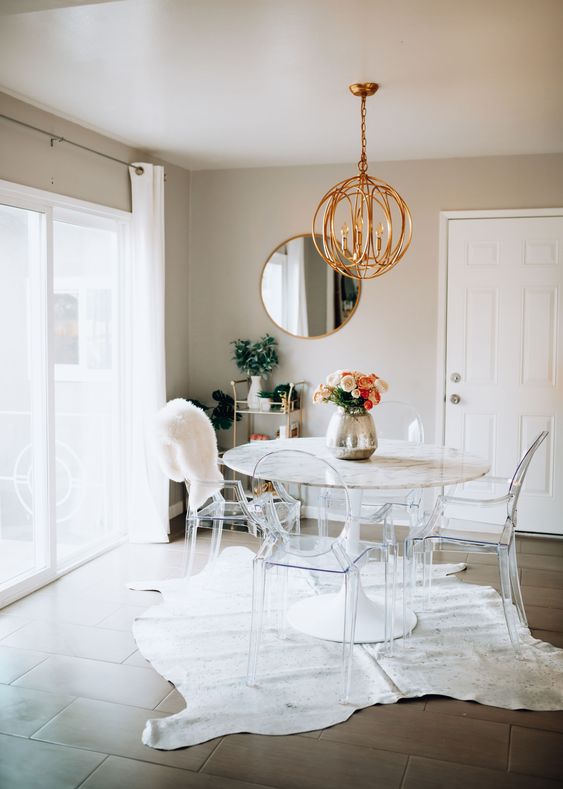a catchy dining space with greige walls, a round table, ghost chairs, a copper sphere pendant lamp and a small cart in the corner