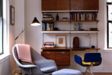 a catchy mid-century modern living room with a stained wall-mounted shelving unit, a blue chair, a grey Wumb chair and ottoman, a printed rug