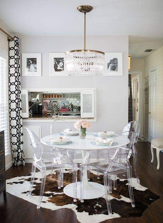 a catchy modern farmhouse dining space with a round table, ghost chairs, a cowhide rug, a crystal chandelier and a gallery wall