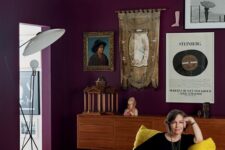 a catchy purple living room with a stained credenza, a mustard chair, a side table, a bold and catchy gallery wall and a floor lamp