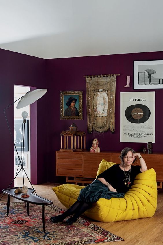 a catchy purple living room with a stained credenza, a mustard chair, a side table, a bold and catchy gallery wall and a floor lamp