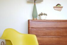 a catchy space with a rich-stained dresser, a yellow Eames rocker, a table lamp, a quirky clock and a basket