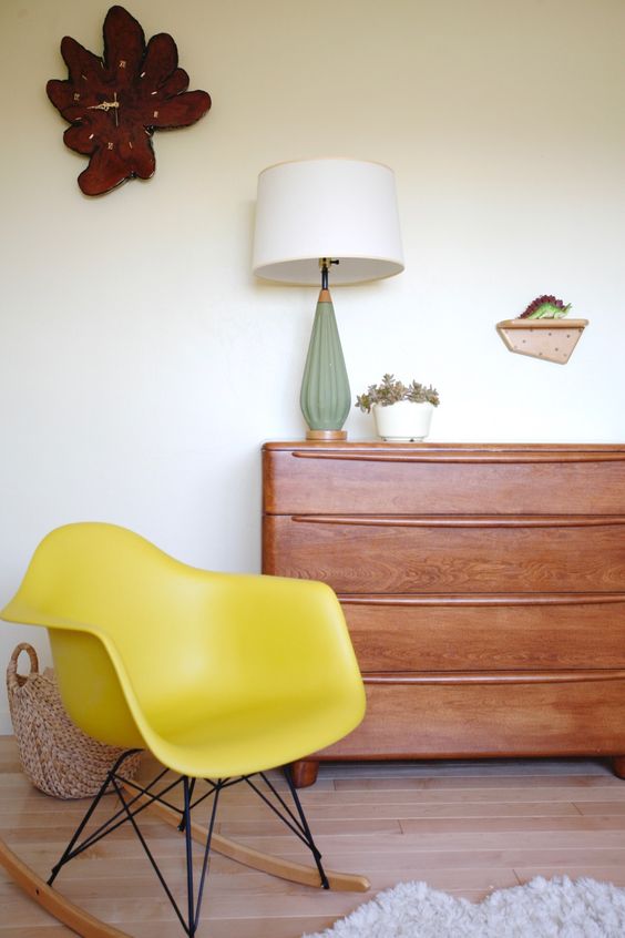 A catchy space with a rich stained dresser, a yellow Eames rocker, a table lamp, a quirky clock and a basket
