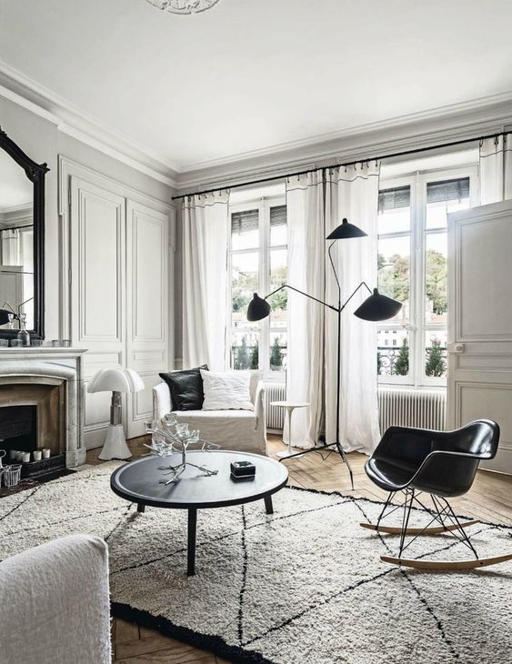 a chic Scandinavian living room with a non-working fireplace, a black coffee table and a black rocker chair, a black floor lamp