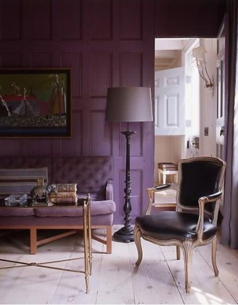 a chic and refined living room with a purple accent wall, a purple sofa and a black leather chair, a coffee table and a floor lamp