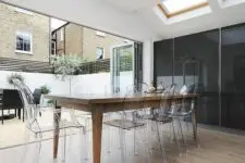 a chic and stylish dining room that can be opened to outdoors, with skylights, a stained dining table, ghost chairs is a lovely and elegant space