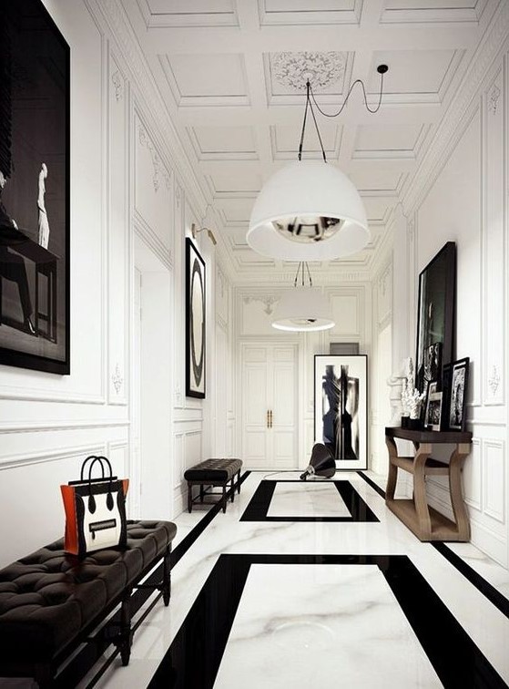 a chic black and white entrance with white walls and a marble floor, artworks and a mirror in a frame, black leather benches