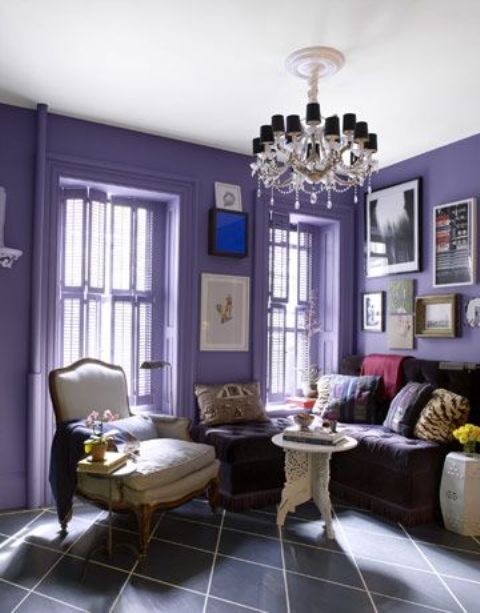 a chic lilac living room with a deep purple sofa, a neutral chair and a carved table, a glam chandelier and a gallery wall