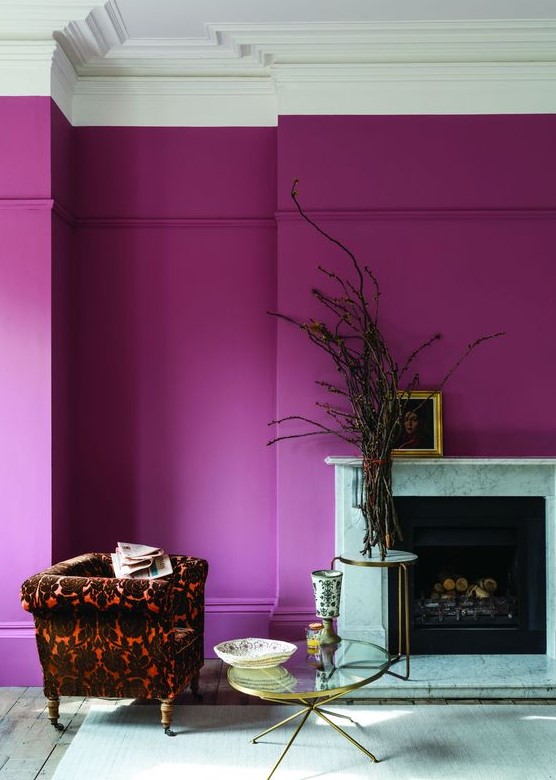 a chic living room with a purple accent wall, a fireplace, a printed chair, mini coffee tables and branches plus some art